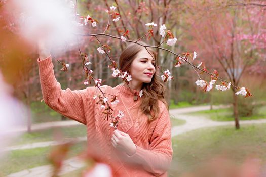 a woman standing under a pink blossoming sakura branch looks away. copy space
