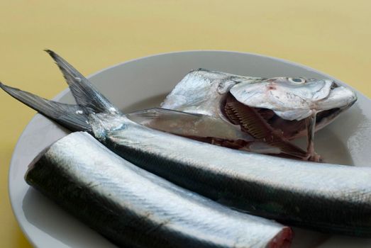 Preparing fresh fish with the head and tail on a plate in the process of being cleaned for the kitchen