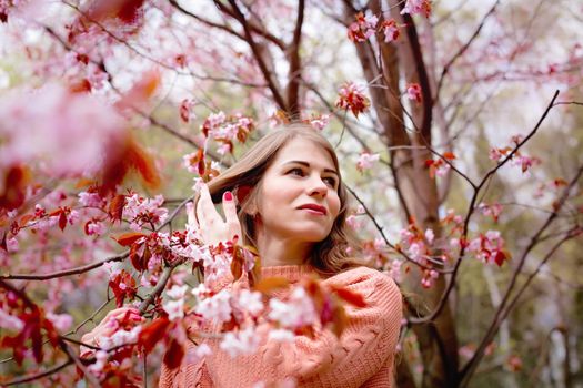 Beautiful woman standing under a pink flowering tree in a spring park. Copy space
