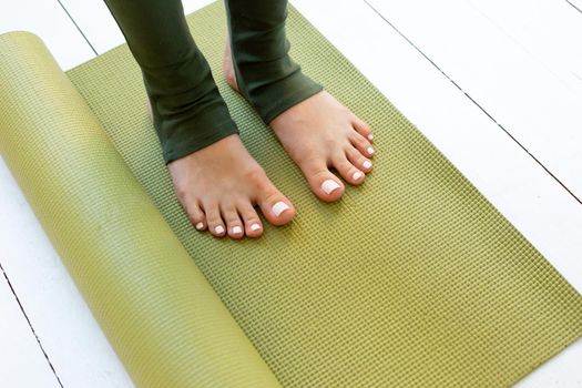 Female beautiful feet in green leggings on green rubber sports mat or fitness mat lying on white floor. Copy space