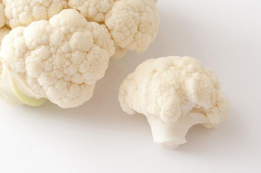Focus to a single floret of fresh uncooked white cauliflower with additional florets alongside ready for cooking as a tasty healthy vegetable accompaniment