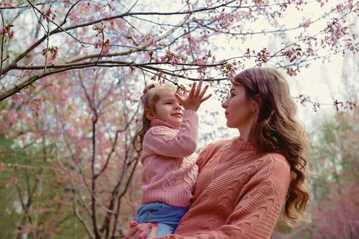 Mother and little daughter are standing in the park, in spring, under cherry blossoms. Close. copy space