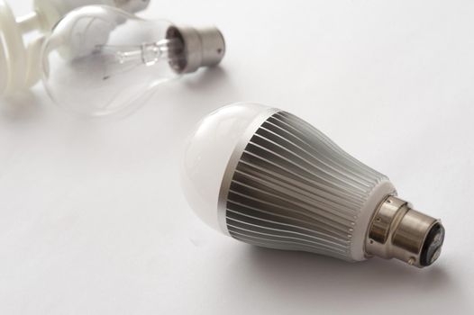 heatsink on a bayonet cap LED energy efficient light bulb, with older incandescent lamp and CF lamp in the background