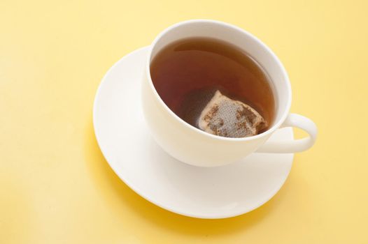 High angle view of a freshly brewed cup of black tea with a teabag inside steeping to the right strength on a yellow background with copyspace