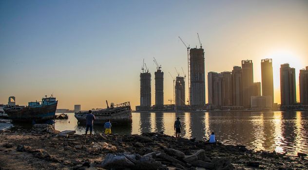 Sunrise in Jadaf area of Dubai, view of Dubai creek Harbor construction of which is partially completed. Old abandoned ships can be seen on the scene. Some men fishing. Outdoors