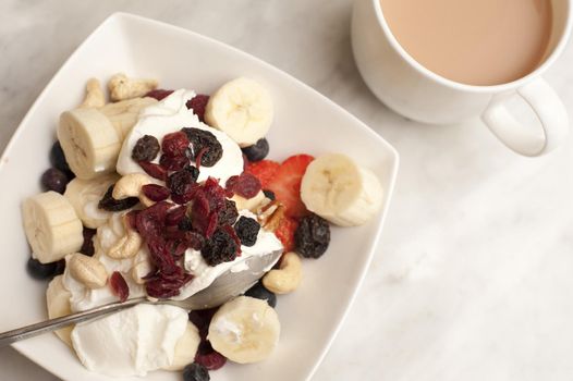 Tea and healthy breakfast cereal topped with yoghurt , raisins and sliced fresh strawberry and bananas, high angle view