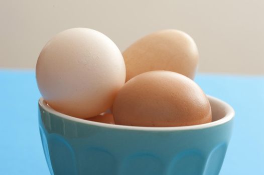 Fresh whole raw brown and white hens eggs in a blue ceramic bowl on a blue kitchen table in a close up view