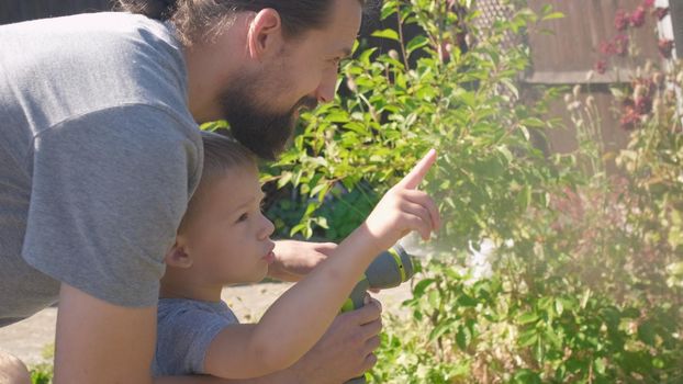 Father and Son. Funny little boy watering lawn plants in garden housing backyard with Dad. Summer house work. Hardworking preschool Kid outdoors. Children help with housework. activity for kids.