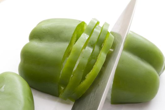 Slicing fresh green capsicum, bell pepper or sweet pepper with a sharp kitchen knife during preparation for salads, close up view of the blade of the knife and vegetable