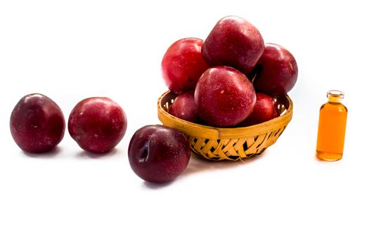 Raw organic red ripe plums in a brown-colored basket along with its extracted essential oil in a small transparent bottle isolated on white.Easy to cut and remove from the background and to use it.