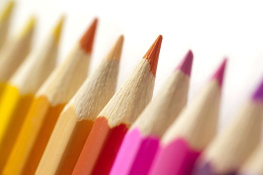 Colorful line of wooden pencil crayons arranged magenta through red to yellow with focus to the central red crayon