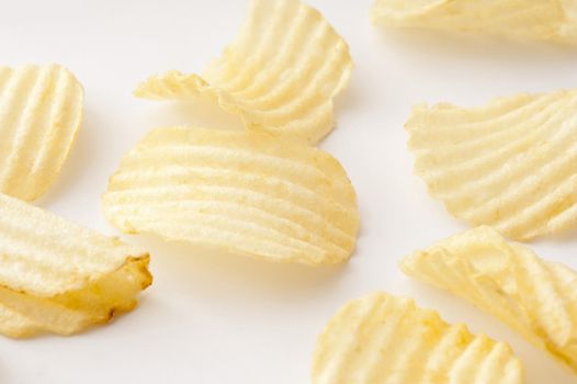 Close up view on various sized scattered ridged potato chips over white background surface