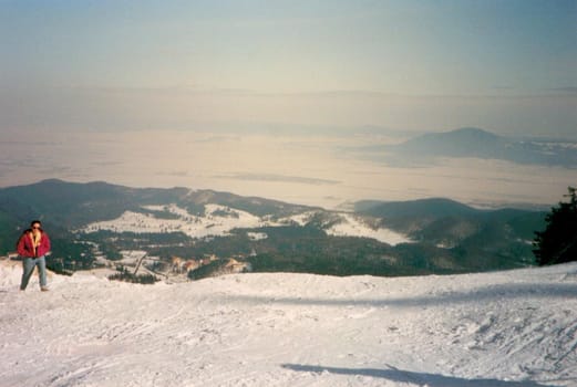 Man walking on a snow-capped mountain plateau or summit overlooking distant snowy mountain ranges on a sunny winter day