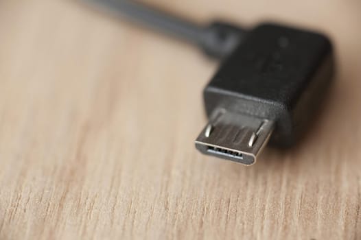 Micro USB connector with black wire, close-up macro shot on wooden table with copy space