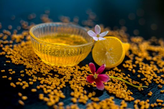 Famous natural method for dandruff on wooden surface in a glass bowl consisting of fenugreek seeds powder well mixed with lemon juice.With raw lemons and fenugreek seeds on the present on the surface.