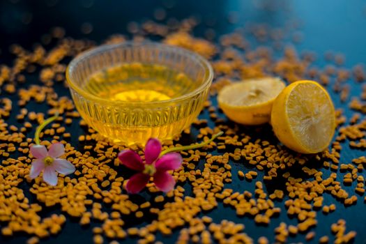 Famous natural method for dandruff on wooden surface in a glass bowl consisting of fenugreek seeds powder well mixed with lemon juice.With raw lemons and fenugreek seeds on the present on the surface.