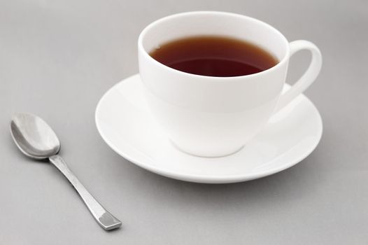Generic white cup and saucer of hot black tea with a teaspoon alongside over gray