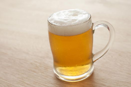 Large cold clear glass tankard of frothy beer, draft or lager standing on a wooden pub or bar counter with copyspace