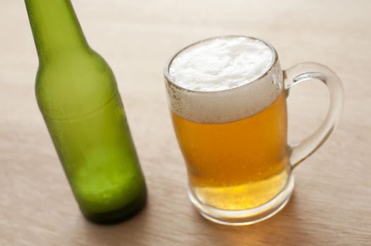 Close up high angle view of a glass tankard and unlabelled green bottle of cold beer on a wooden bar counter