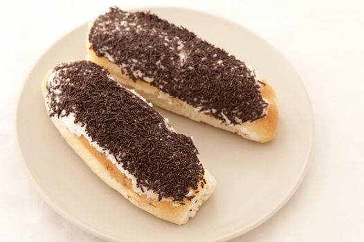 Two sticky buns glazed with creamy icing and topped with chocolate sprinkles served on a plate for a tasty teatime treat