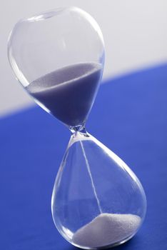 Tilted angle view of sand running through an hourglass over a blue and grey background measuring the passage of time