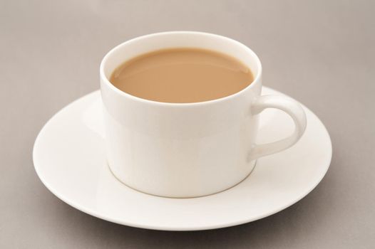Cup of coffee with milk on saucer standing on grey table