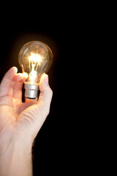 a hand holding a glowing lightbulb with space for copy on a black background