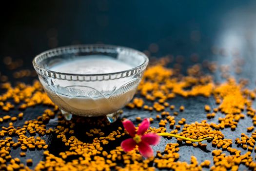 A famous natural method for dandruff on wooden surface in a glass bowl consisting of fenugreek seeds powder well-mixed with curd in a glass bowl.Along with raw curd and fenugreek seeds on the surface.