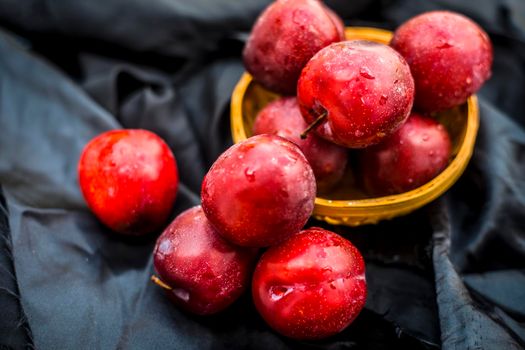 Raw organic red ripe plums in a brown-colored basket on black fabric on the wooden surface.