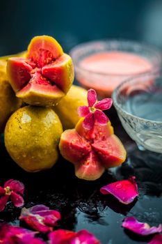 Guava pulp and water well mixed in a glass bowl on the wooden surface along with some raw cut guava, with some rose petals, also completing a face mask used for a natural glow.