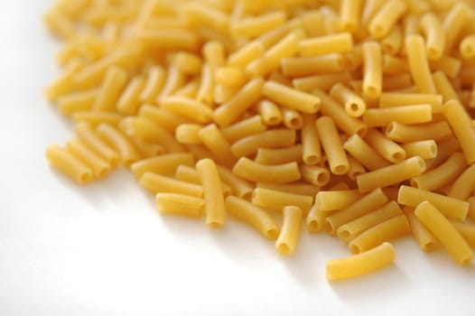 Heap of dried macaroni pasta for Italian and Mediterranean cooking on a white background with copyspace