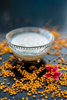 A famous natural method for dandruff on wooden surface in a glass bowl consisting of fenugreek seeds powder well-mixed with curd in a glass bowl.Along with raw curd and fenugreek seeds on the surface.