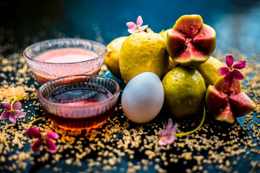 Treatment of dry skin with the help of face mask on a wooden surface consisting of honey, guava pulp, egg yolk, and some oatmeal, well mixed in a glass bowl along with raw ingredients.