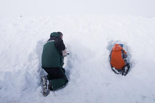 A boy and his father digging the snow cave.