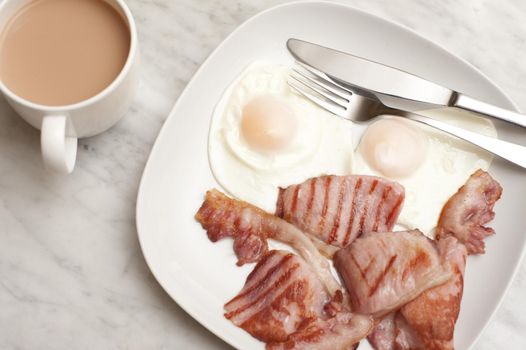Serving of two fired eggs and tasty rashers of grilled bacon for breakfast with a cup of freshly brewed coffee