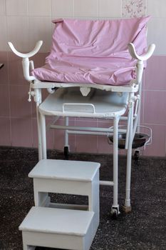 Image of old pink gynecological chair in toffice room professional clinic with copy space. Pregnancy Planning parturition lying-in maternity pain obstetrics Concept.
