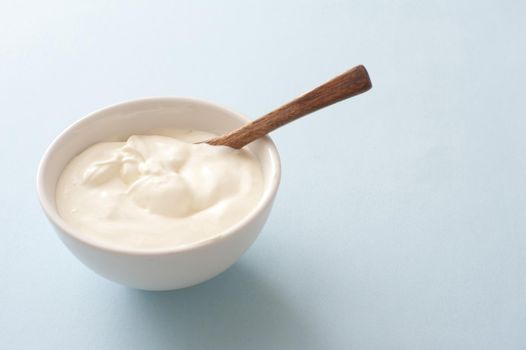 Bowl of fresh sour cream with spoon and copy space over a light grey background to be served as an accompaniment or topping