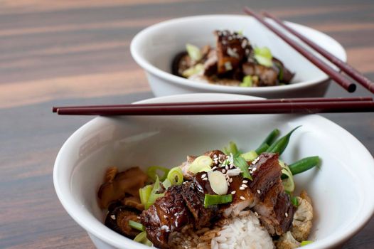 Close up of a bowl of Chinese fatty pork and vegetables topped with a rich sauce and served with chopsticks