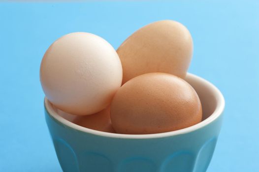 Little blue bowl of brown eggs over matching color background for concept about farm fresh food