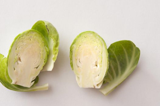 Fresh green Brussels sprout head cut in half, viewed in close-up on white surface background