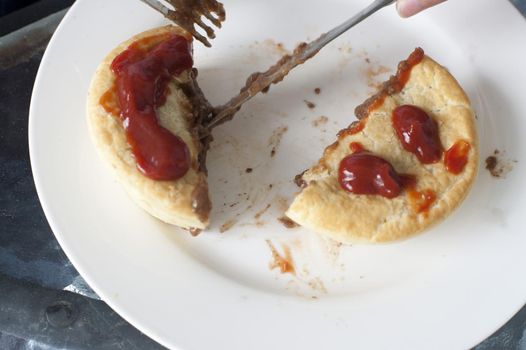 High angle view of a person eating a savory meat pie for lunch with gravy on the pastry crust cutting it with a knife and fork