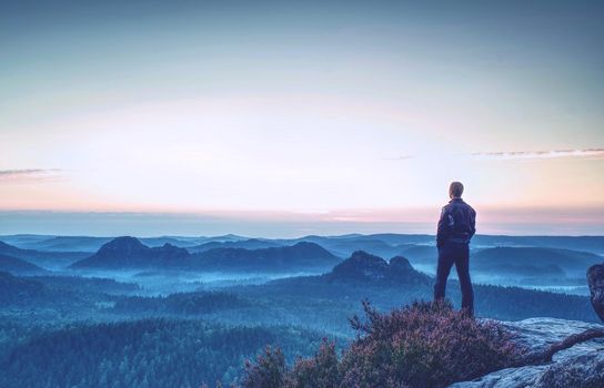 Hiker stands and enjoys valley view from hilly viewpoint. Hiker reached top of the mountain and watching sunset.