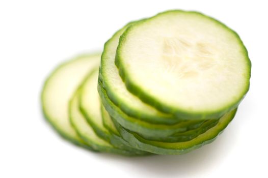 Stacked sliced cucumber with focus to the top slice showing the fleshy pulp and green rind on white