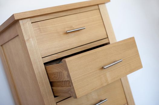 Small wooden chest of drawers or cabinet with metal handles and one open drawer, tilted angle view