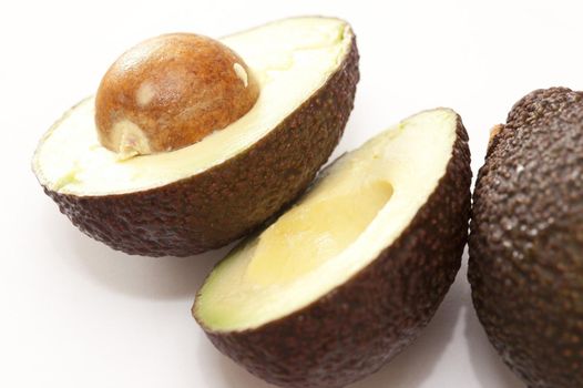 Halved and whole fresh avocado pear with the pip showing the texture of the soft tasty fleshy pulp on a white background