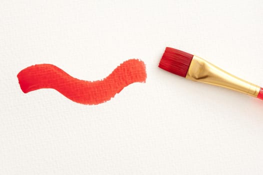 Single plastic and copper paint brush with red curving stroke over textured white paper