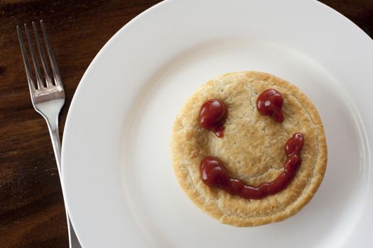 Happy meat pie with a smiley face formed of rich brown gravy on top of the pastry crust, overhead view on a plate