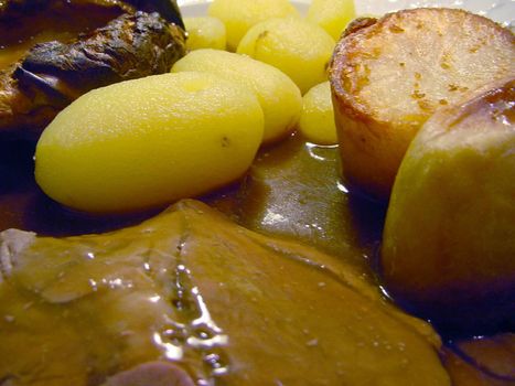 Close up of a serving of traditional English sliced roast beef, potato and Yorkshire Pudding topped with gravy