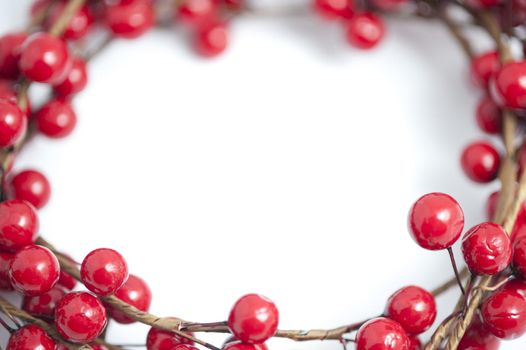 Border, wreath or frame of artificial festive red Christmas berries around central white copy space for your holiday message