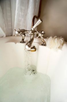 Closeup of a retro combination metal tap fitting with hot water flowing while running a relaxing bath